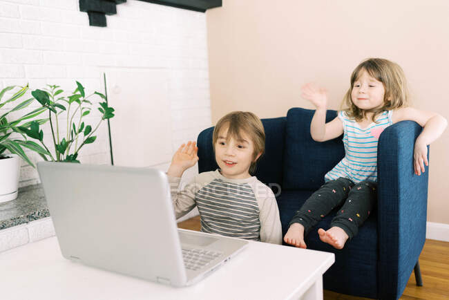 Двое маленьких детей за ноутбуком в гостиной во время видеозвонка в Интернете — стоковое фото