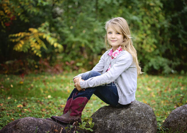 Giovane bionda ragazza in rosso cowboy stivali seduto fuori su una roccia — Foto stock