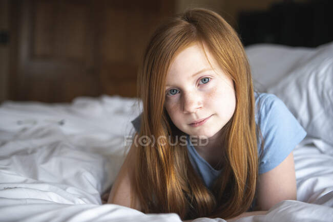 Beautiful girl in a white shirt lies on a sofa in the bedroom with a pillow. — Stock Photo