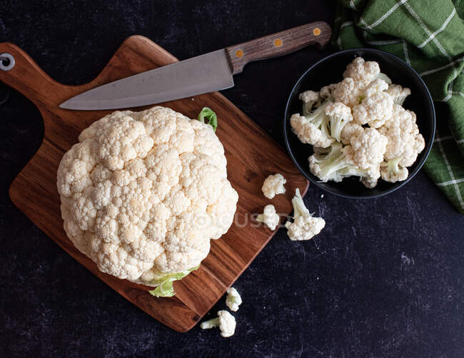 Cauliflower and florets on cutting board and in bowl on black counter. — Stock Photo