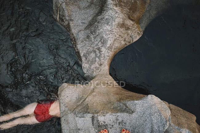 Женщина в красном костюме плавает в темной воде. Вид сверху — стоковое фото