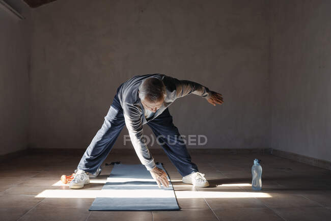Uomo anziano che fa esercizi di stretching e di allenamento con i pesi a casa — Foto stock
