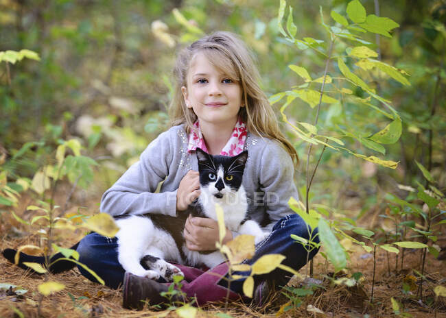 Joven rubia sentada en el bosque con gato blanco y negro en el regazo. - foto de stock