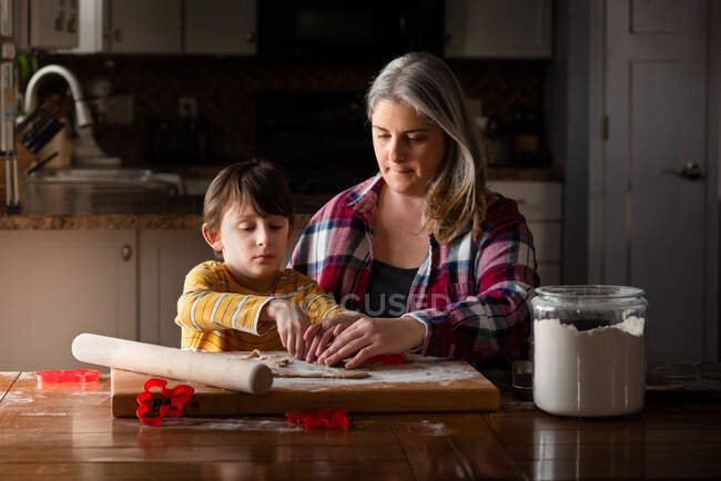 Una madre y un hijo horneando galletas juntos en la mesa de la cocina - foto de stock