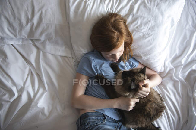 Junge Frau mit niedlichem Kätzchen, das auf dem Bett liegt und sich umarmt. glückliche Familie mit Katze im Zimmer. — Stockfoto