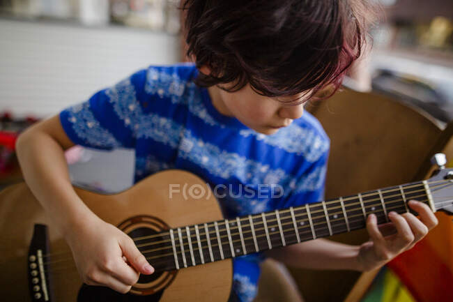 Tween menino ternamente toca uma guitarra acústica na varanda da frente de casa — Fotografia de Stock