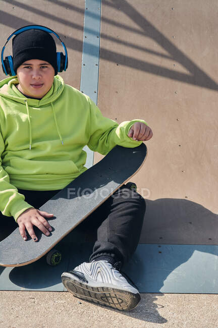 Молодий, підліток, з скейтбордом, сидячи на доріжці, з навушниками — стокове фото