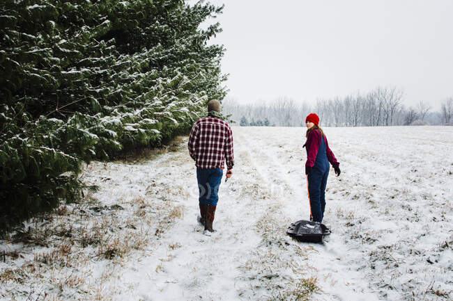 Dos adolescentes caminando por un campo cubierto de nieve con pinos en Michigan - foto de stock