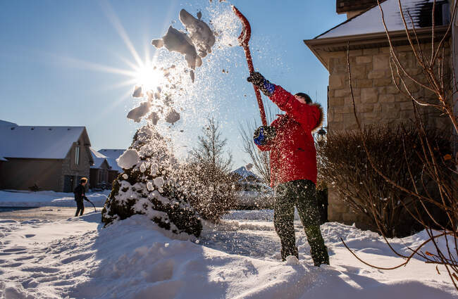 Niño de abrigo rojo paleando nieve de la pasarela de su casa. - foto de stock