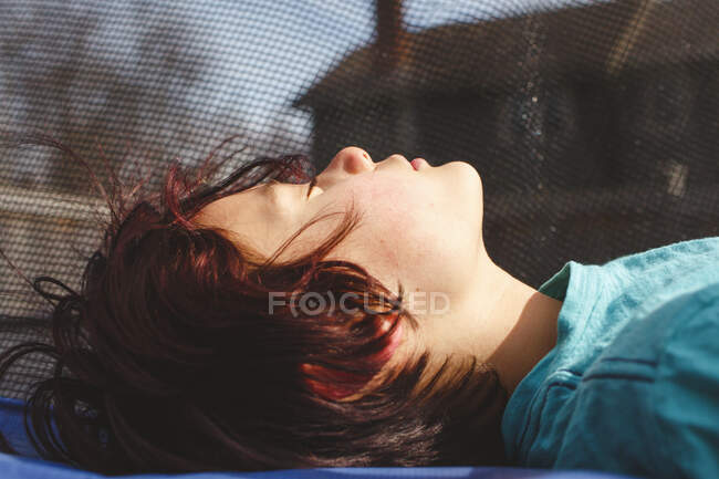 Gros plan de tween garçon étendu sur un trampoline sous le soleil chaud — Photo de stock