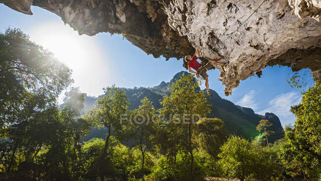 Людина, яка піднімається на навислу вапнякову скелю в Лаосі. — стокове фото