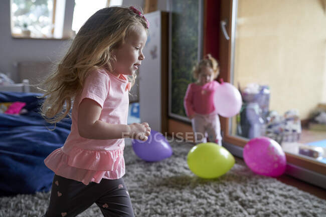 Feliz niña corriendo por casa y jugando con su hermana y sus bolas. - foto de stock