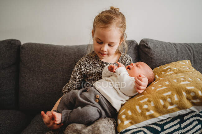 Beautiful white girl holding newborn baby brother on the couch at home — Stock Photo