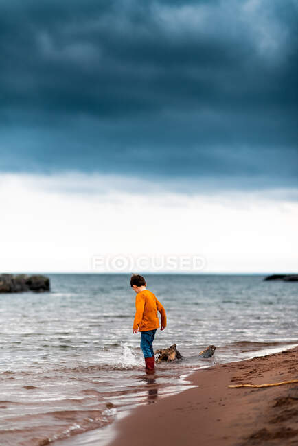 A small boy splashing his foot at the shoreline of lake superior — Stock Photo
