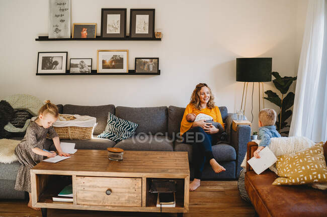 Happy mom in living room breastfeeding baby and talking to older kids — Stock Photo