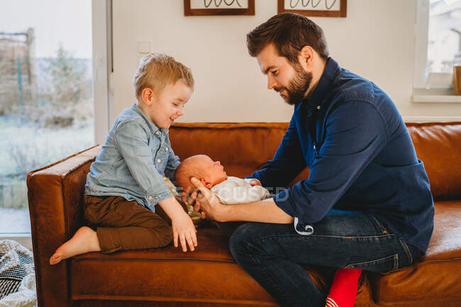 White dad and son smiling at newborn baby on sofa at home — Stock Photo