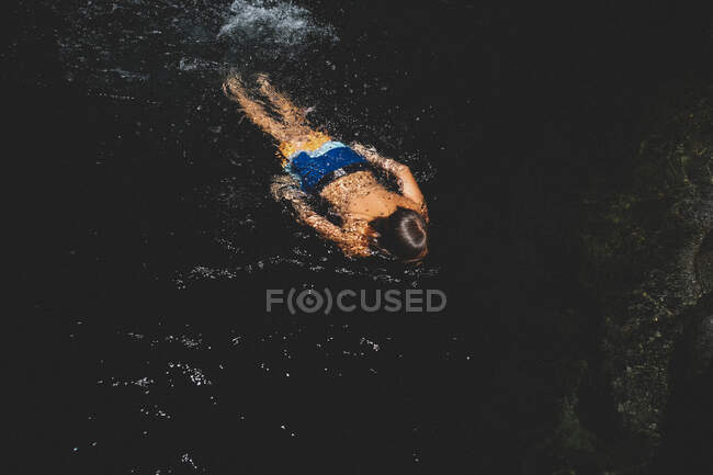 Junge in heller Badehose schwimmt und planscht in dunklem Pool — Stockfoto