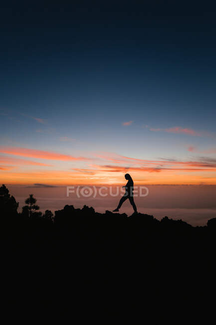 Mujeres caminando sobre roca en acantilado contra el cielo al atardecer - foto de stock