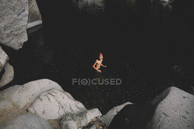 Дистанційний постріл хлопчика з рожевим волоссям, що стоїть у темній воді — стокове фото