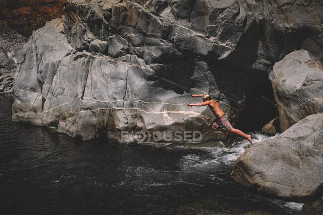 Menino salta para o buraco de natação fluindo água e granito Canyon Walll — Fotografia de Stock