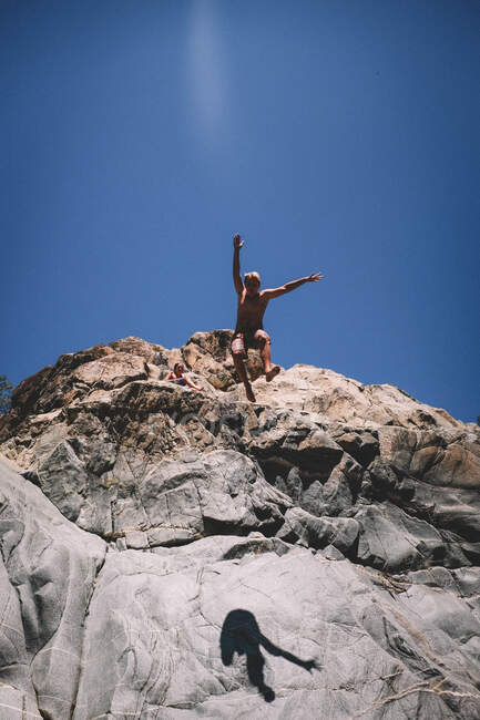 Adolescente menino saltos de penhasco com azul céu atrás dele — Fotografia de Stock