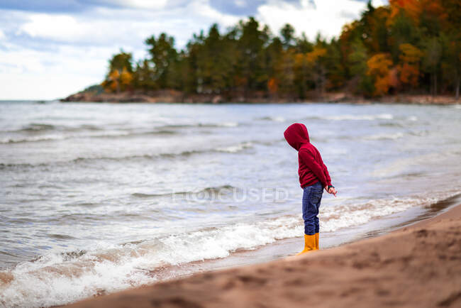 Boy standing on shore line of Lake Superior looking down at water — Stock Photo