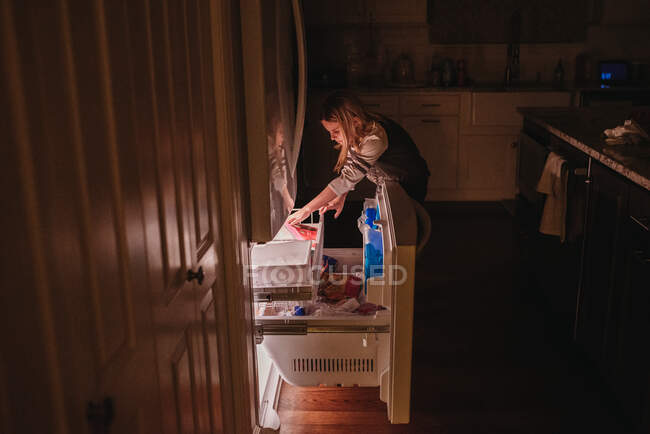 Tween chica llegar en congelador cajón en oscuro cocina - foto de stock