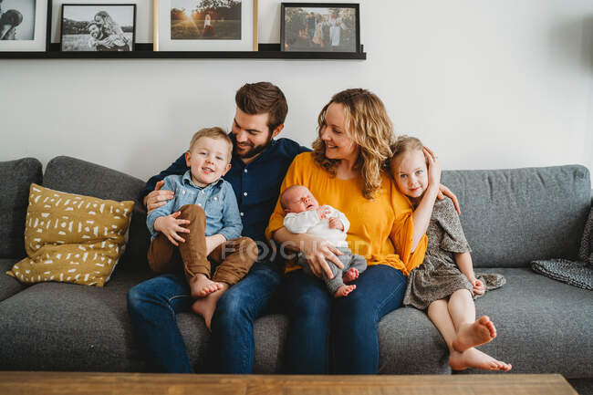 Хорошо выглядящая счастливая белая семья, держащая новорожденного ребенка на диване дома — стоковое фото