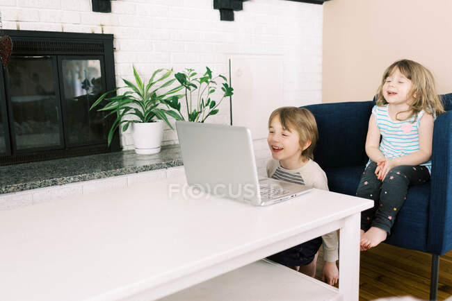 Двое маленьких детей за ноутбуком в гостиной во время видеозвонка в Интернете — стоковое фото