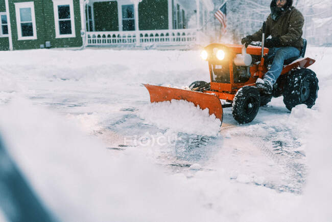 Mann auf Traktor pflügt während eines Ostersturms Schnee in einer Einfahrt — Stockfoto