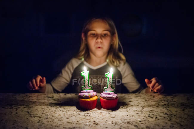 Девочка-подросток задувает свечи на двух кексах с несобранным лицом — стоковое фото