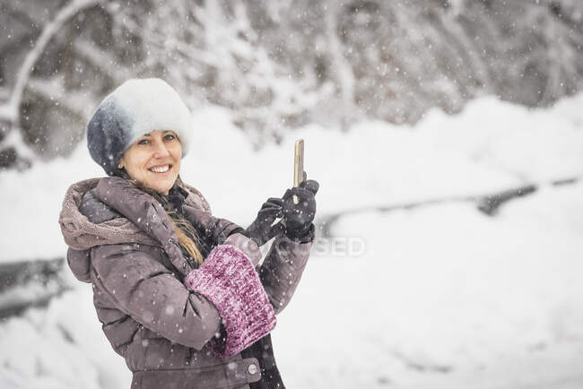 Femme avec bonnet de neige prenant un selfie au milieu d'une chute de neige — Photo de stock