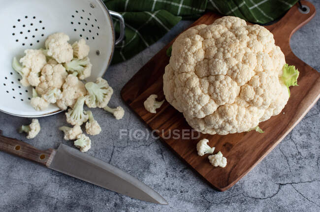 Cauliflower and florets on cutting board and colander on gray counter. — Stock Photo