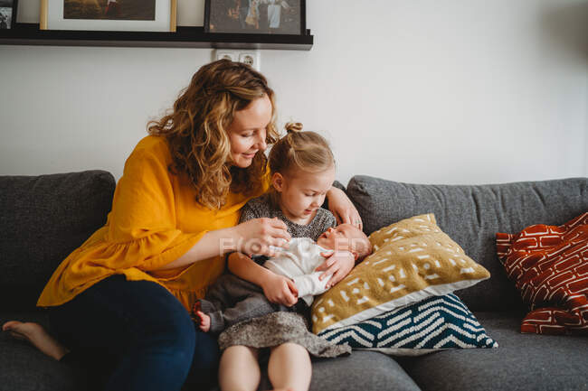Mutter und Tochter sitzen auf Sofa und halten Baby im heimischen Wohnzimmer — Stockfoto