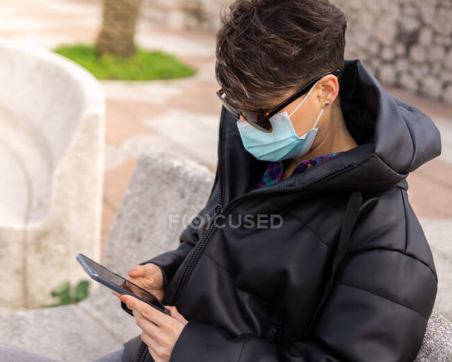 Frau mit kurzen Haaren und Maske plaudert mit Telefon — Stockfoto