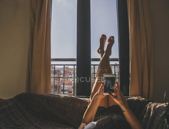Молодая женщина лежит на диване с поднятыми ногами и фотографирует — стоковое фото