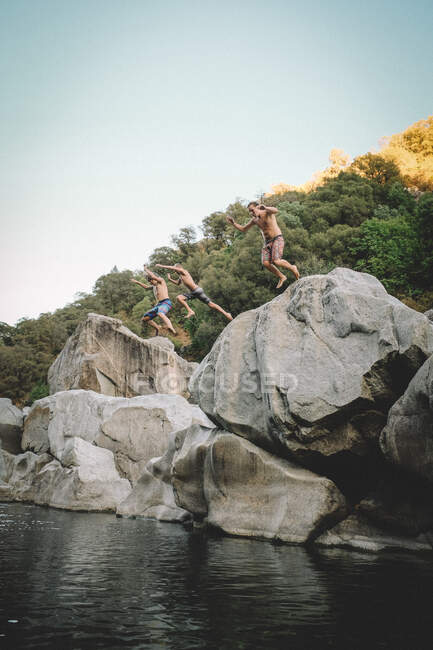 Tres chicos saltan a un charco de agua al atardecer - foto de stock
