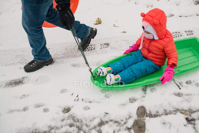 Маленького ребенка тащит в санях папа во время снежной бури — стоковое фото