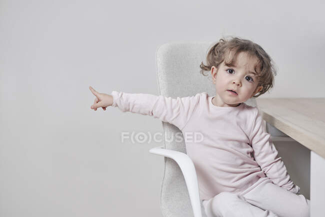 Une fille de 2 ans pointe du doigt quelque chose où elle s'assoit. — Photo de stock