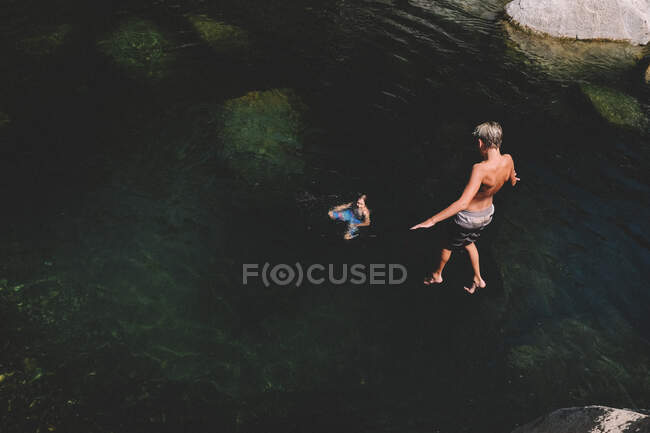 Boy Hovers Mid Jump Enquanto seu amigo olha para a água abaixo — Fotografia de Stock
