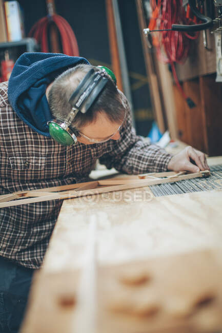 Un uomo caucasico di mezza età lavora su un piccolo pezzo di aeroplano di legno nel suo garage. — Foto stock