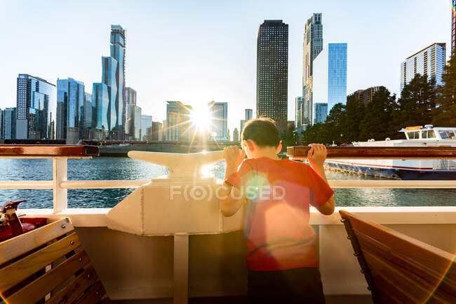 Un niño en un barco mirando al agua con el horizonte de la ciudad de Chicago - foto de stock