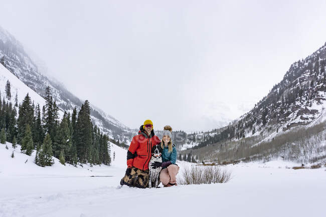 Glückliches Paar mit Hund auf schneebedecktem Feld gegen den Himmel im Urlaub — Stockfoto