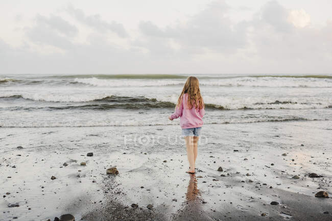 Young girl standing at the waters edge at the beach — Stock Photo