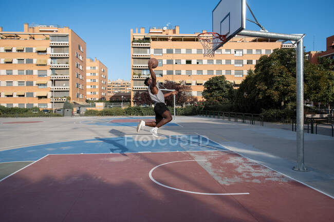 Афроамериканский игрок прыгает и бросает мяч в обруч на баскетбольной площадке — стоковое фото