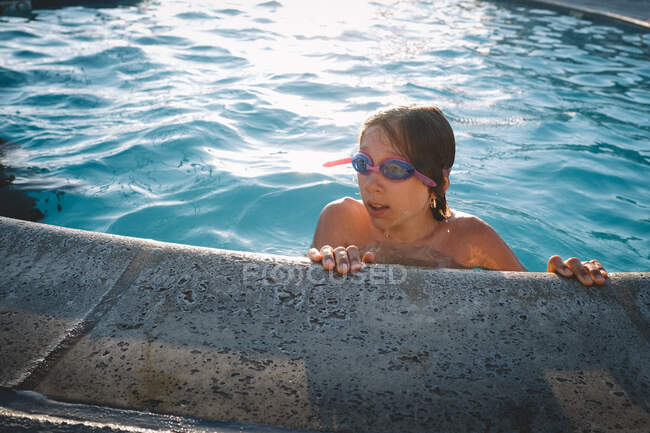 Boy in Goggles Pops his His out of a swimming pool at day's end - foto de stock