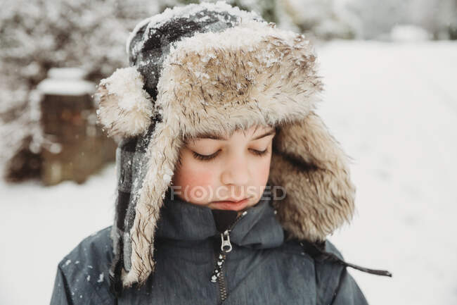 Портрет хлопчика, який дивиться вниз в пухнастому капелюсі в снігу — стокове фото