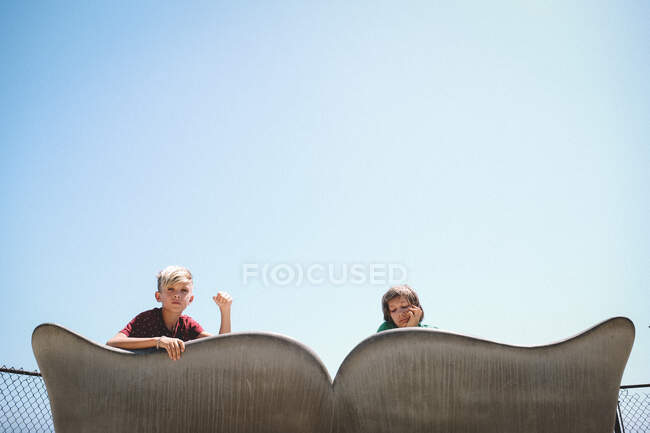 Chicos echan un vistazo sobre un banco de cuento de ballenas de cemento en un día de verano - foto de stock