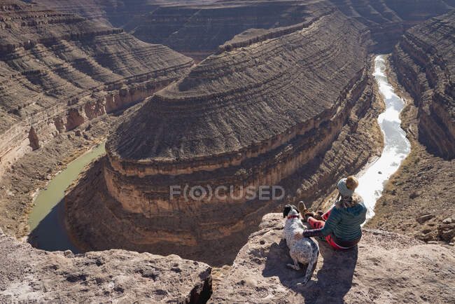 Donna seduta con cane guardando la vista dalla scogliera a Goosenecks State Park durante le vacanze — Foto stock