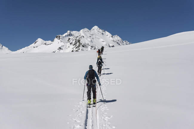 Visão traseira de machos e fêmeas com placas divisórias andando na montanha coberta de neve contra o céu claro — Fotografia de Stock